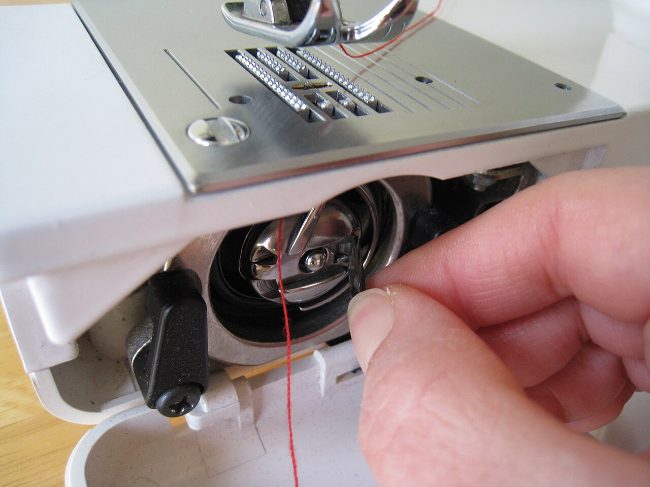 Hand removing a bobbin case from the hook area of a sewing machine