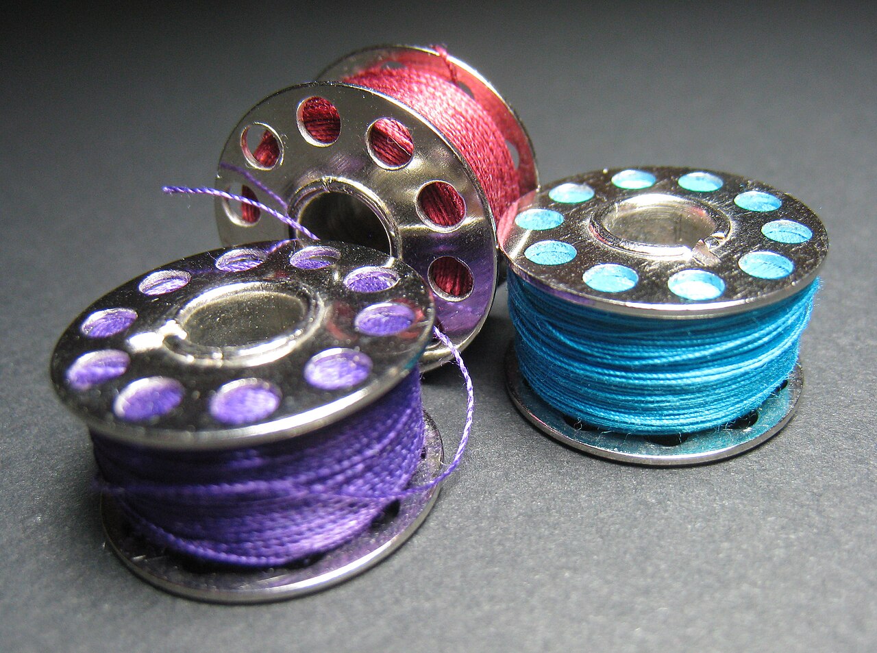 Three metal bobbins wound with purple, red and blue thread
