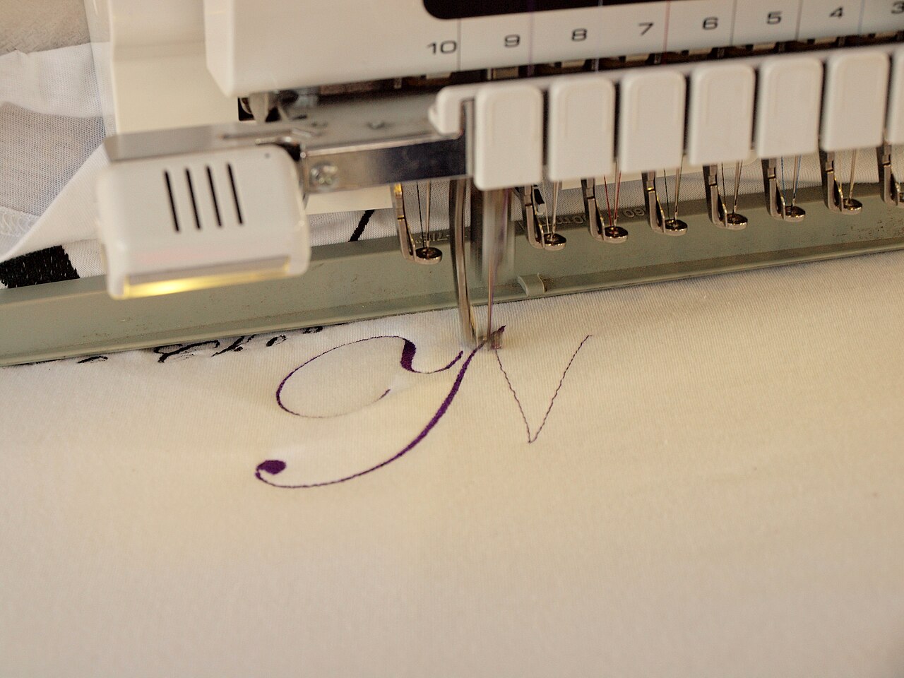 Close-up of numbered needle bars on a multi-needle embroidery machine sewing a letter
