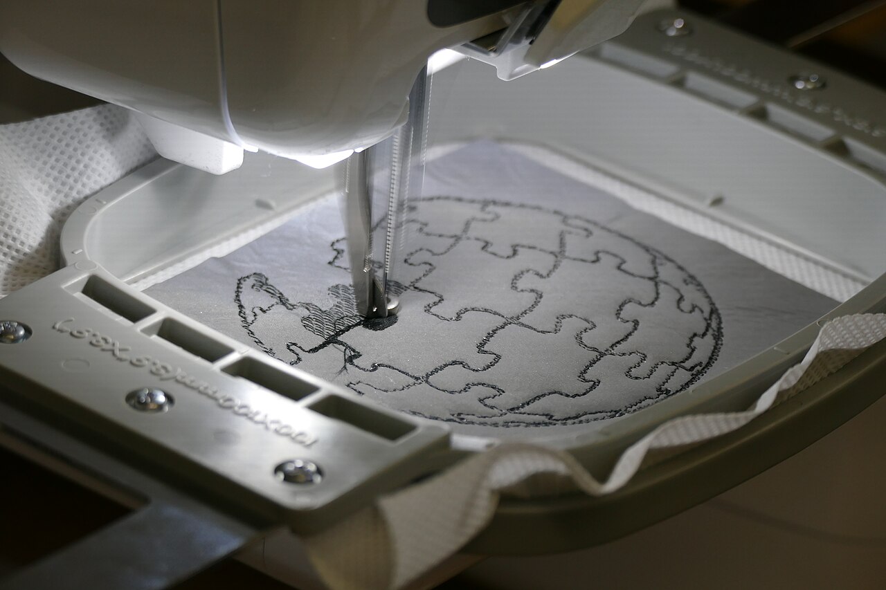 Embroidery needle stitching an outline design inside a hoop
