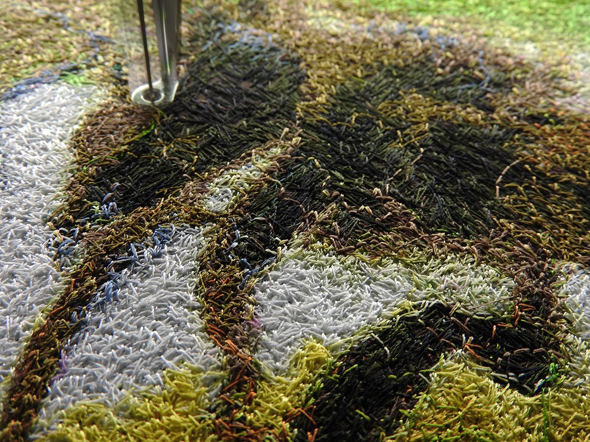 Close-up of dense multicolour embroidery stitches with a needle above