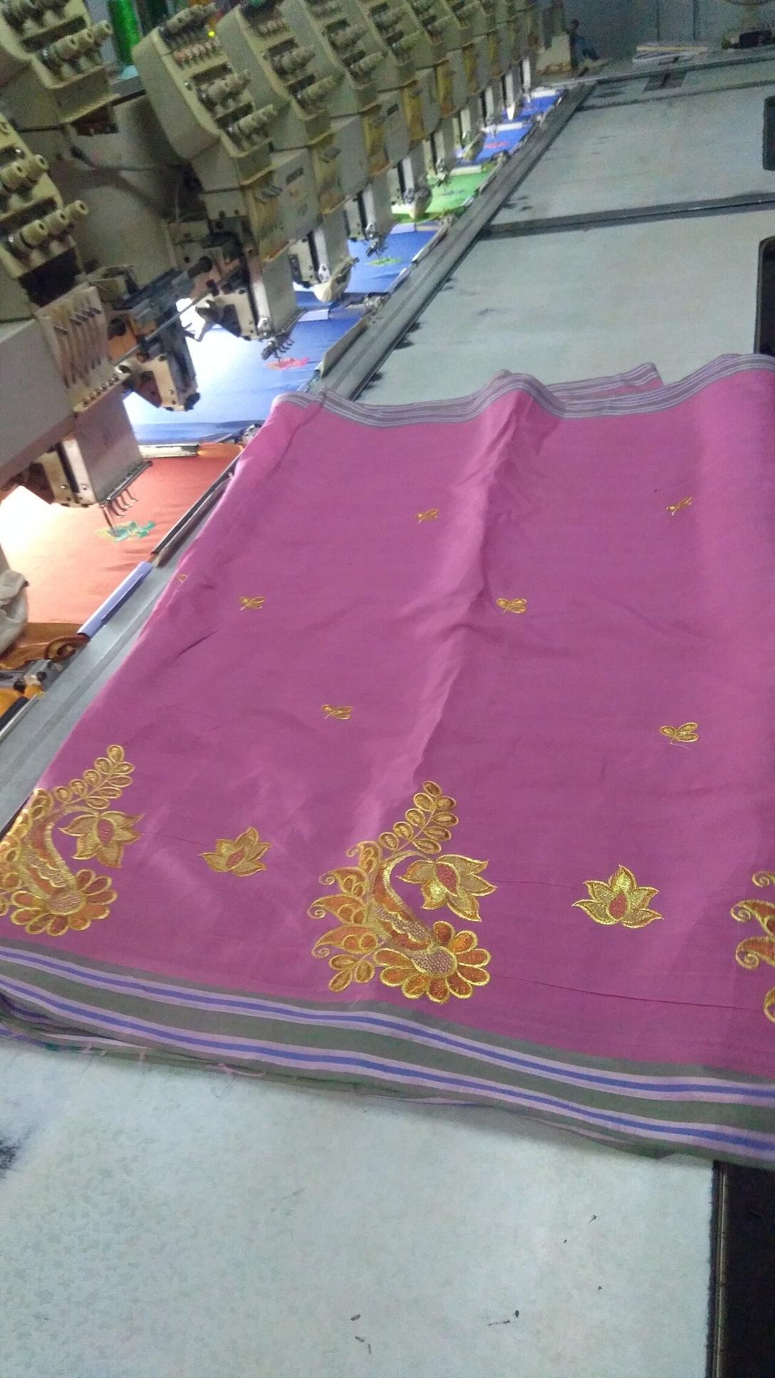 Row of embroidery heads stitching gold floral motifs onto pink fabric