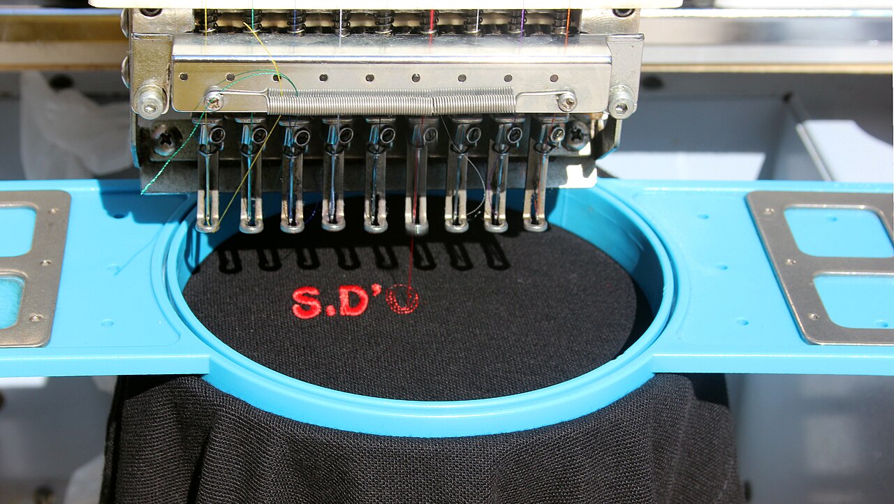 Multi-needle embroidery head over a blue hoop on black fabric