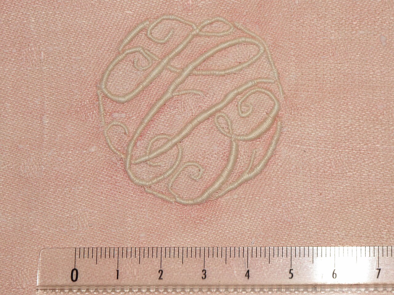 Raised satin-stitch monogram next to a centimetre ruler