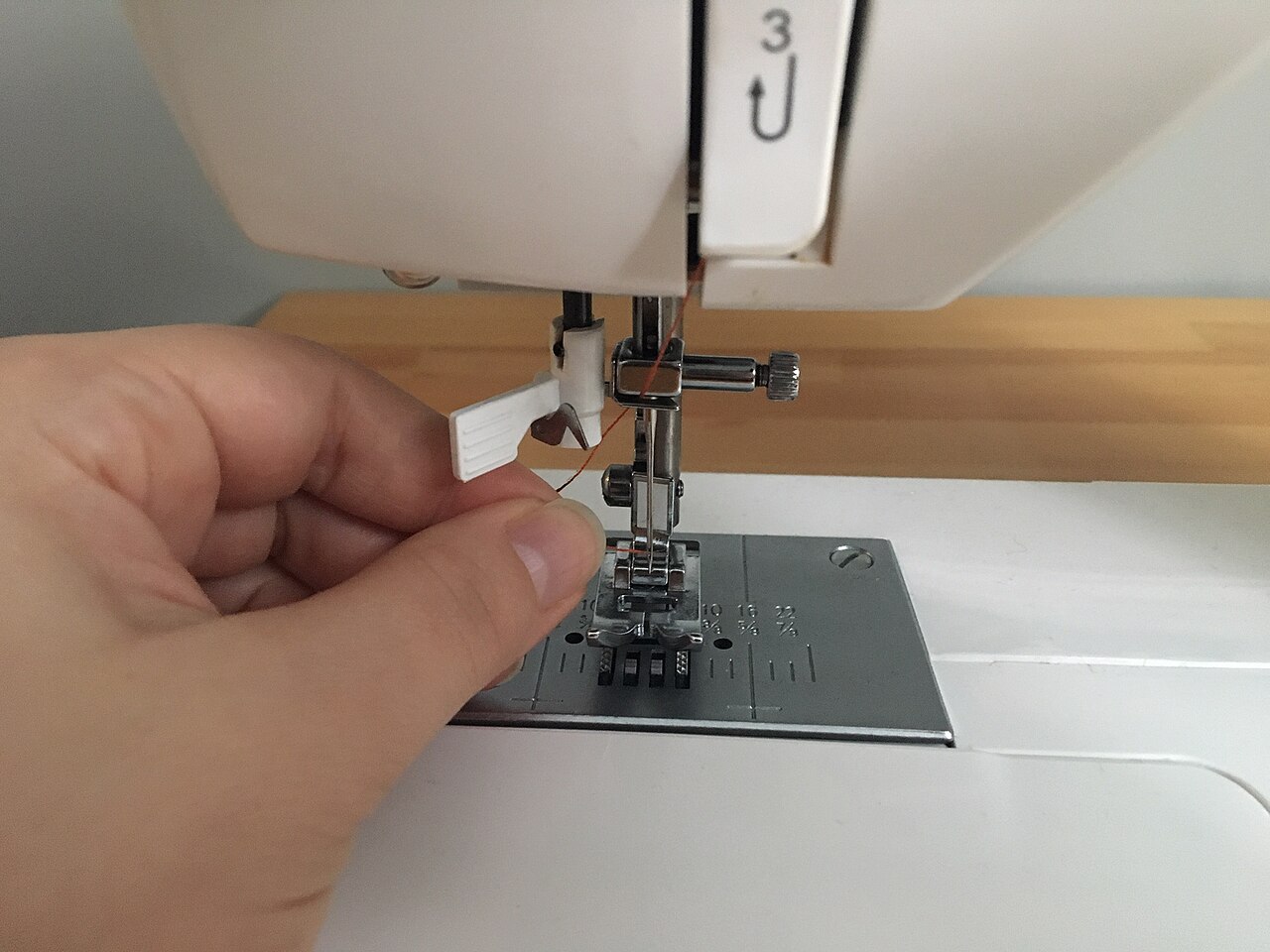 Hand guiding thread into the tension discs of a sewing machine